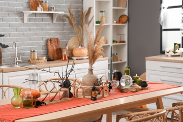 Dining table with Halloween decor and burning candles in kitchen