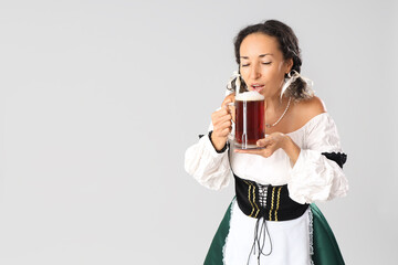 Beautiful mature happy Octoberfest waitress with mug of beer on grey background