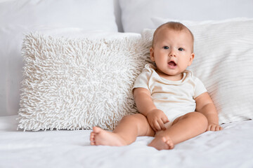 Cute little baby sitting on bed in room at home