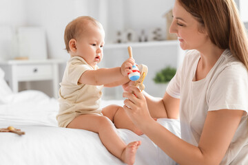 Beautiful young happy mother with cute little baby and rattles sitting in bedroom at home