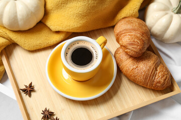 Cup of tasty pumpkin coffee with croissants and warm plaid on bed at home