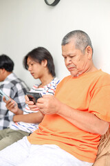 Fototapeta premium Modern Asian Father And His Two Son Using Mobile Phone Playing Games Together