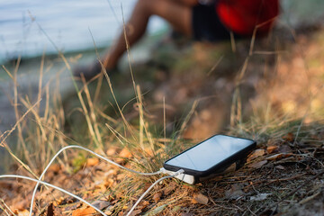 The portable charger charges your smartphone in nature, with a backdrop of a camper and a lake.
