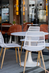 Cozy outdoor cafe restaurant terrace with empty white chairs in autumnal city. Modern lounge outside with relaxed atmosphere. Exterior cozy patio