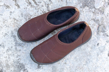 A pair of fashionable and comfortable ladies shoes, used but still durable, rest on a concrete floor.