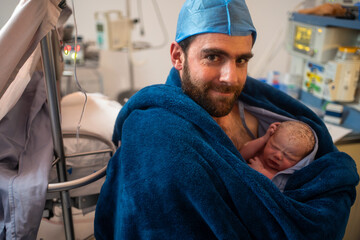 smiling father holding his newborn baby after caesarean section surgery in the hospital operating...
