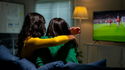 Two women on sofa watching football match on tv