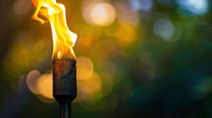 A close-up of a burning tiki torch with a blurred background of out of focus greenery and lights.