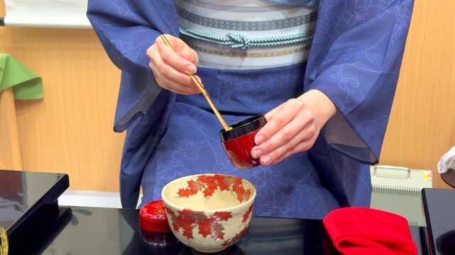 Matcha, finely powdered green tea, is prepared by woman in serene Japanese tea ceremony, where precision of whisking creates rich, smooth beverage, steeped in centuries-old tradition.