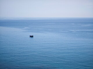 Obraz premium a single boat on a vast expanse of water, likely an ocean or large lake. The water is calm with minimal wave activity, and the horizon line is visible in the distance. The sky appears clear