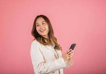 Fototapeta premium Happy Asian portrait beautiful business young woman teen smiling excited using smart mobile phone studio shot isolated on pink background, Thai female surprised making winner gesture on smartphone