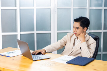 Asian businessman working in his office reviewing work, accessing planning strategy, creative thinking and innovation ideas, sitting at his desk using laptop computer, professional business worker.