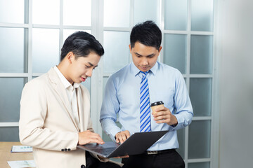 Asian businessmen working together in an office using technology devices, planning strategy, creative thinking innovation ideas, assisting helping each other with teamwork communication skills.