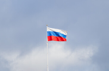 Russian tricolor flag waving in the wind against a blue sky.