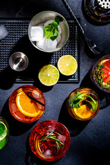 Alcoholic cocktails, top view. Set of colorful drinks for party. Black background, bar tools, hard light, top view