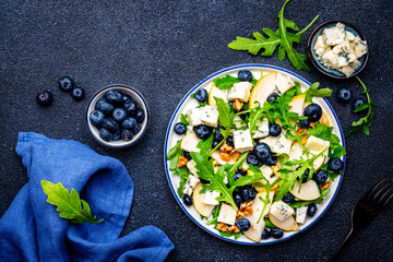 Tasty salad with pears, blueberries, roquefort cheese, arugula and nuts. Black background, top view