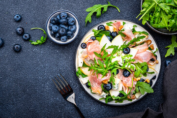 Foodie food salad with pears, blueberries, gorgonzola cheese, smoked ham, arugula and walnuts. Black background, top view