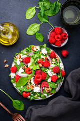 Foodie food salad with fresh raspberries, feta cheese, onion, walnuts and spinach, black background, top view