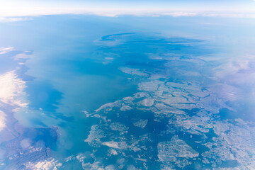 View from the airplane window at a beautiful blue clear sky, earth, sea and the airplane wing