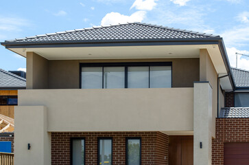 The front facade of a new modern, two-story suburban house in Australia features a balcony with sliding glass doors and a concrete railing. Concept real estate, housing, and a future home.