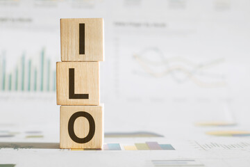 Wooden alphabet cubes form the abbreviation ILO on an office desk against a backdrop of business...