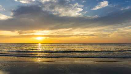 Beautiful sunset above sea or ocean and reflection of sun in the water and sand on beach.