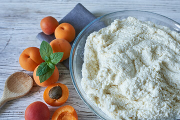 A bowl of cottage cheese and apricots on a wooden table. Preparation of dough for a pie.