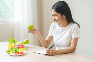 Diet, happy asian young woman working, write diet plan right nutrition holding green apple with eat...