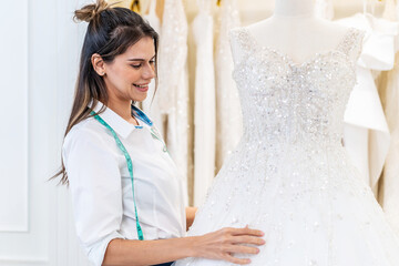 Smiling caucasian woman is bridal shop owner tidying up the wedding dress in office room at wedding studio, Small business entrepreneur wedding planner and tailor designer concept