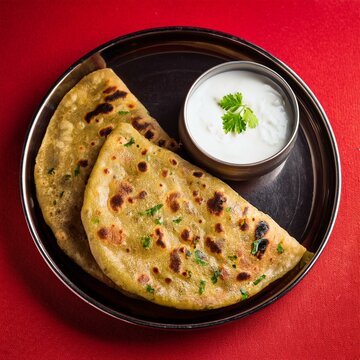 Indian traditional breakfast food aloo paratha is a potato stuffed flatbread served with curd on red background