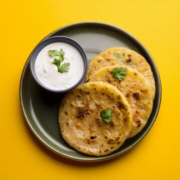 Indian traditional breakfast food aloo paratha is a potato stuffed flatbread served with curd on yellow background
