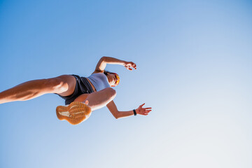 Young female athlete leaps over a hurdle in a parkour workout under a clear blue sky