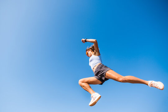 Young female athlete leaps over a hurdle in a parkour workout under a clear blue sky