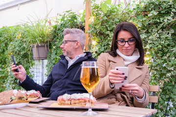 Couple at a restaurant table, engrossed in their smartphones during lunch, illustrating the impact of technology addiction on a couple
