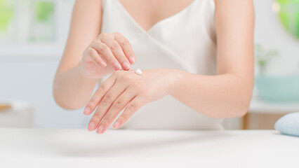 A woman applies a small amount of moisturizer to the back of her hand, showcasing a gentle skincare routine. The image exudes a fresh, minimalist feel, and personal care in bathroom background.