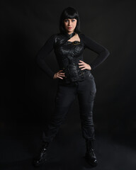Full length portrait of beautiful black female model with short black hair wearing sci fi futuristic dystopian leather bodysuit costume. Standing pose, isolated dark studio background moody silhouette