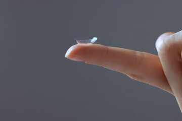 Close-up of finger holding contact lens, on grey background, concept of poor eyesight, astigmatism,...