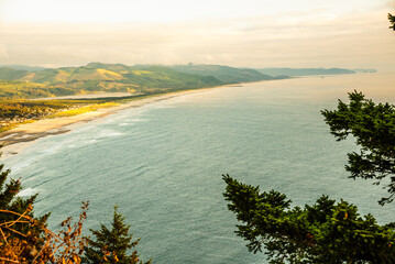 Obraz premium Aerial view of the Oregon coast with mountains and a beach at sunset.