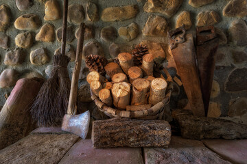 Rural scene with basket of firewood, saws, ax and broom on stone wall background
