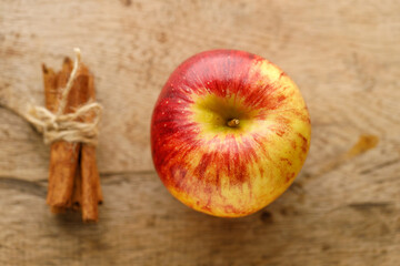 Ripe organic red apple and cinnamon stick on wooden table background.