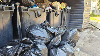 Overflowing black trash bags near public waste bins in a residential area during daylight hours...