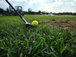 Golfer preparing to swing on a sunny day at a lush green golf course with sprinklers operating