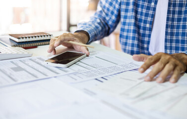 Asian man hand holding pencil using mobile doing online business, checking financial document,...