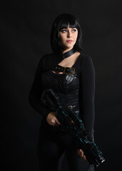 Naklejka premium Close up portrait of beautiful black female model wearing black sci fi futuristic dystopian leather bodysuit costume. holding gun weapon. isolated dark studio background moody silhouette.
