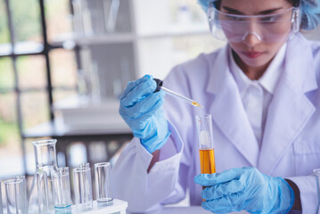 Scientist woman holding chemical test yellow glass tube testing science laboratory. Lab technician holding gold fluid drop to glass tube Urine sample. Asian woman scientist working medical chemistry