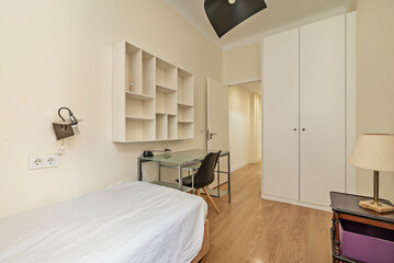 A student bedroom with a desk, white bookshelf and a built-in wardrobe with white wooden doors