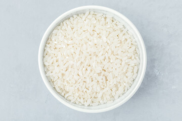 Rice grains. White bowl of raw dry rice on gray stone background, top view. High quality photo
