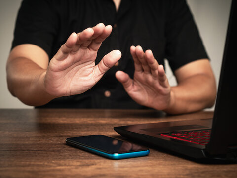 Hands raised in stop gesture near laptop, representing digital pause or work break.