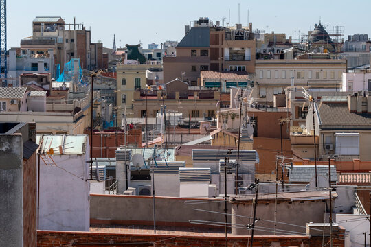 This image captures a densely packed urban scene featuring various rooftops and structures, reflecting a lively city environment under a wide sky filled with chaotic energy in Gracia Barcelona