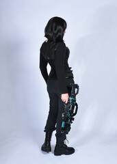 Naklejka premium Full length portrait of beautiful black female model with short black hair wearing sci fi futuristic dystopian leather bodysuit costume. Standing walking pose, isolated white studio background.